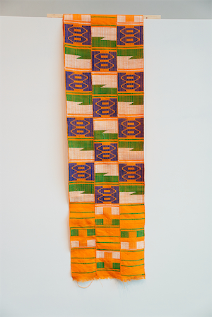A three-paneled handwoven Kente textile from Ghana with alternating strips of warm yellow, blue, aqua, and red overlayed with wavey lines of orange.