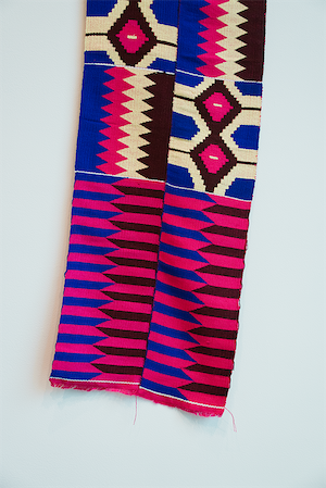 A two-paneled wide handwoven Kente textile from Ghana with alternating tiles featuring zigzags, stripes, and diamond shapes of yellow, orange, aqua, red, and purple.