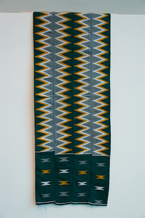 A four-paneled handwoven Kente textile from Ghana with zigzag stripes and geometric patterns of navy, yellow, white, and gray.
