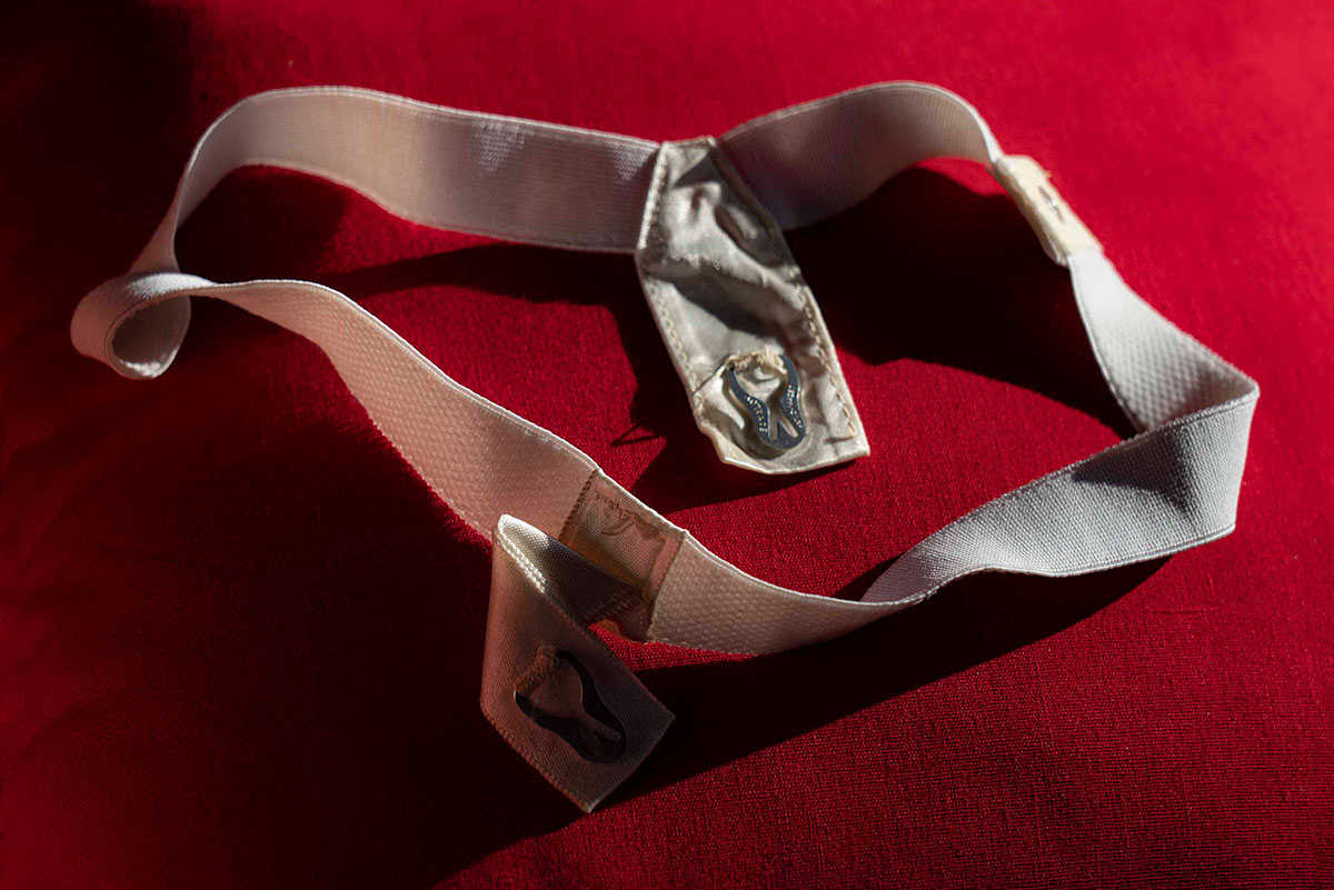 A white vintage menstruation belt lies on a velvety red surface.