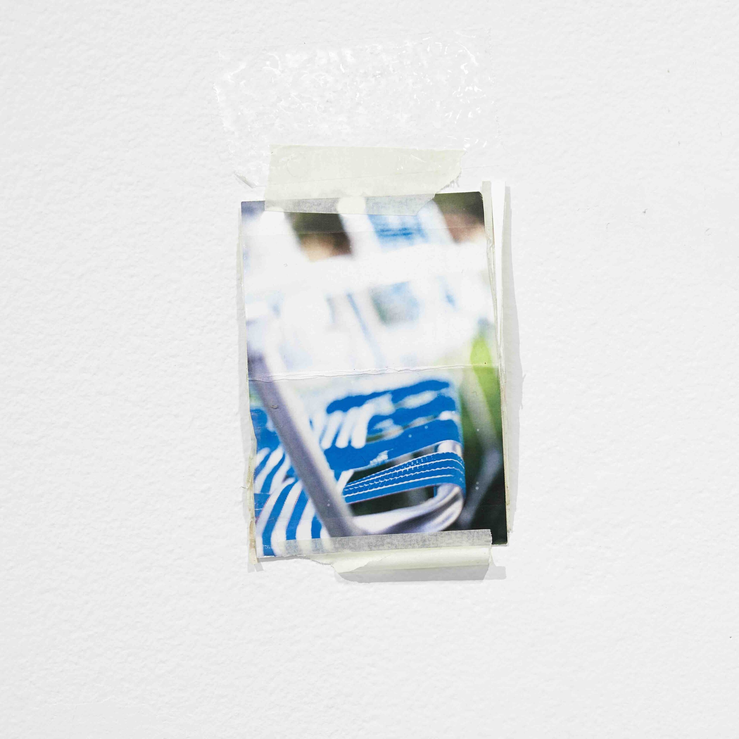 A nearly blurry photograph of a blue lawn chair is taped onto a white wall.