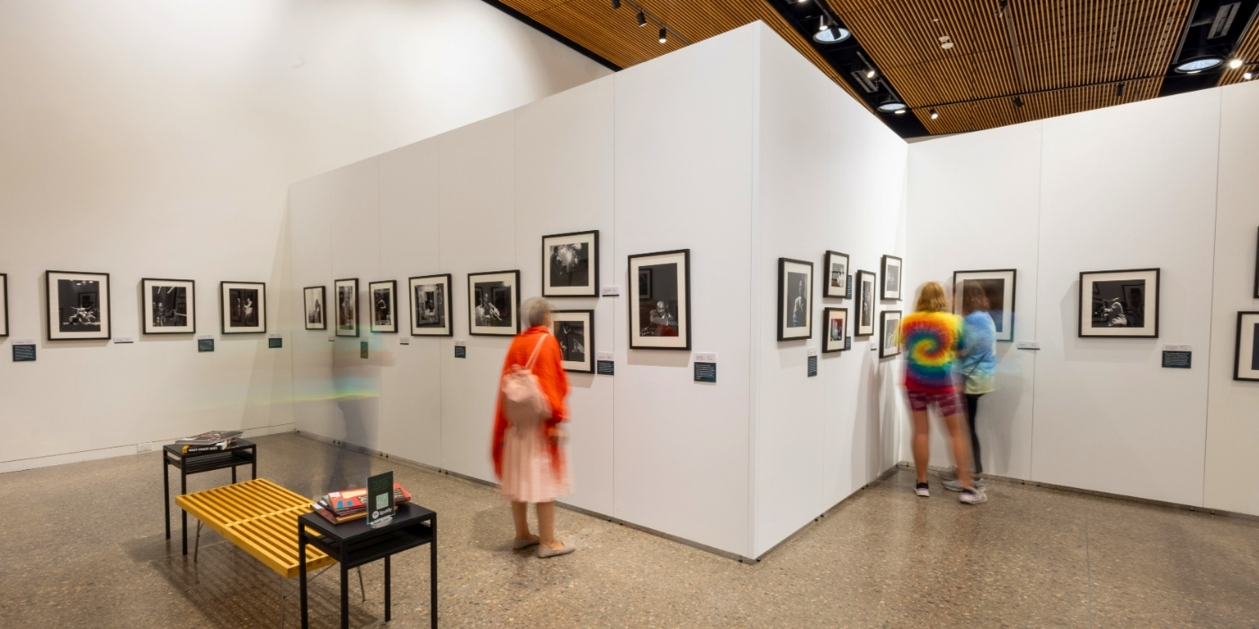 Two people move through a gallery space with photographs on the walls.