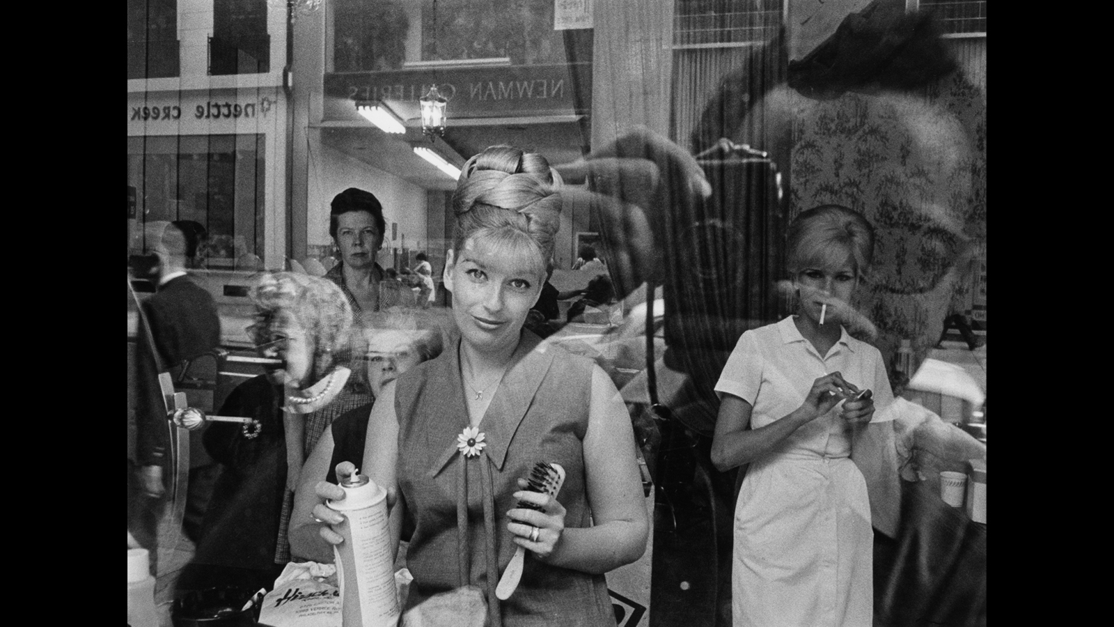 Staff and patrons quizzically look out the window of a beauty parlor while the photographer's reflection is captured in the window.